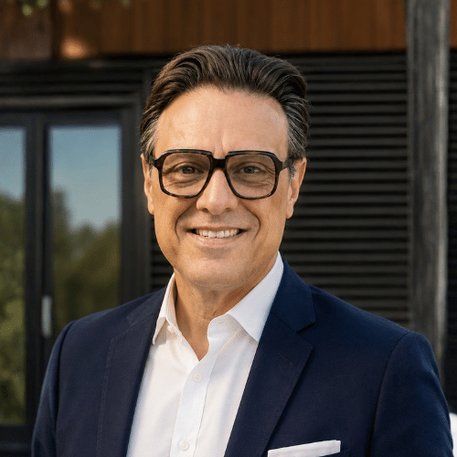 Man with glasses smiling in front of a home